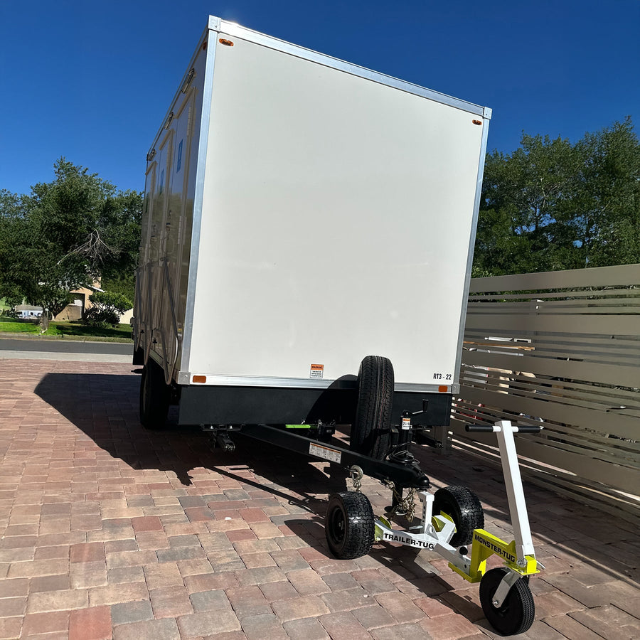 Monster-Tug off-road trailer dolly hitched to the tongue of a white single-axle trailer on a brick driveway under a clear blue sky